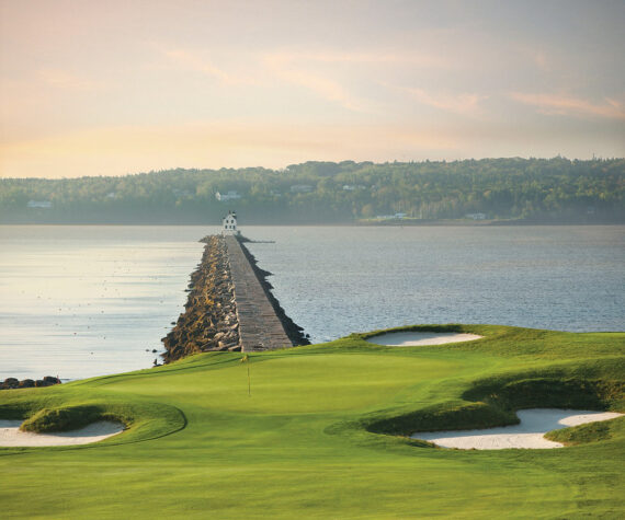Oceanfront golf green with bunkers overlooking a breakwater and lighthouse at golden hour